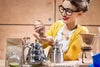 Finding the Best Grinder for Coffee Beans: woman holding fresh coffee beans next to manual grinders and pour-over equipment